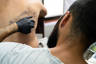 Close-up of artist tattooing on customer back in workshop