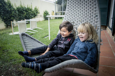 Boy and girl sitting on hanging chair in garden