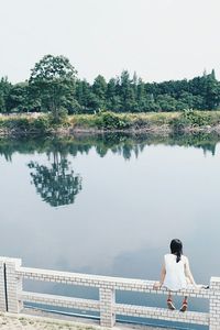 Rear view of people standing by lake against clear sky