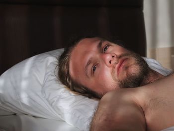 Portrait of shirtless man lying on bed at home