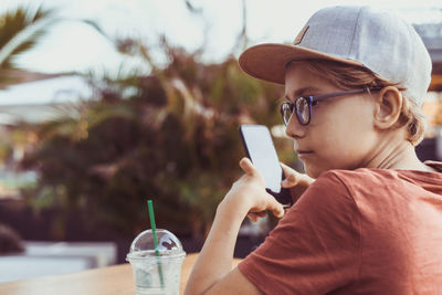 Boy using mobile phone while holding sitting outdoors