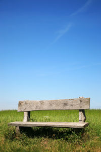 Bench on field against clear blue sky