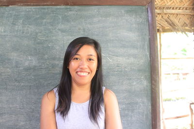 Portrait of young smiling woman against blackboard