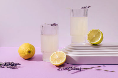 Still life composition with lavender lemonade in ribbed glasses and lemons on purple background