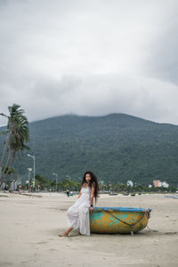 Young woman sitting on beach against sky