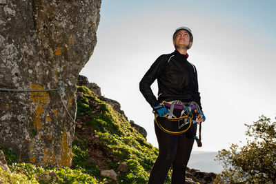 Concept: adventure. climber woman with helmet and harness. pensive standing on a rock. looking at the top of the mountain. solar luminous flare. via ferrata in the mountains.