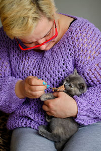 Midsection of a caucasian mature woman feeding little adorable grey kitten with a spoon 