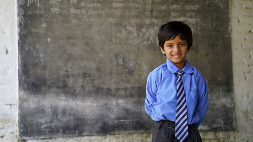 Portrait of happy indian school child sitting at desk in classroom, school kids with pens