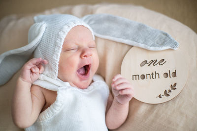 A portrait of a cute newborn baby in a white like a bear cub hat lying on its stomach and laughing