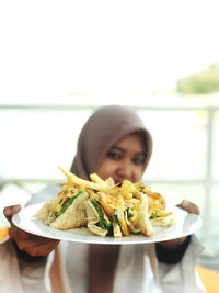 Portrait of woman holding food in plate at cafe