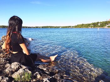 Side view of young woman sitting with pomeranian at lakeshore