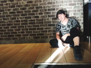 Portrait of man sitting against brick wall at home