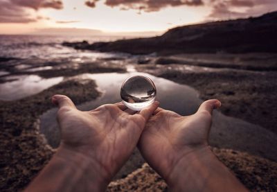 Cropped hands holding crystal ball at beach