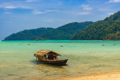 Fishing boat on sea by mountain against sky