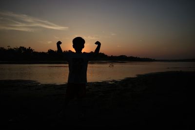 Silhouette man standing at beach against sky during sunset