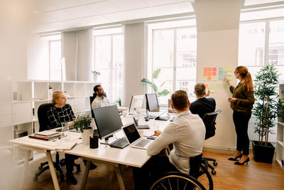 Managers planning sales strategies while discussing over colorful adhesive notes on wall at work place