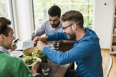 Colleagues at table with cell phone and laptop having lunch