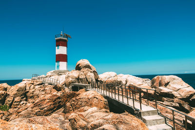 Lighthouse by sea against clear blue sky