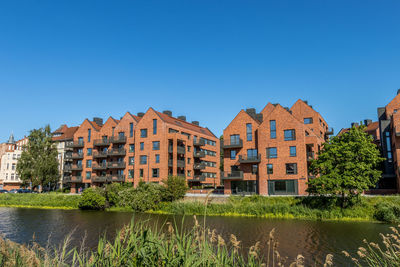 Buildings by the river against clear blue sky