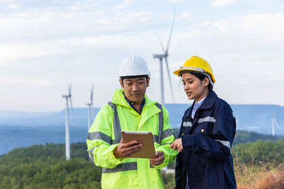 Engineers using digital tablet standing against wind turbine