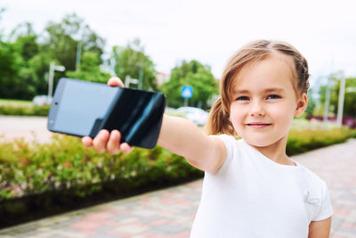 Portrait of cute girl holding mobile phone on footpath