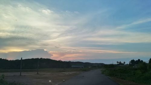 Road by field against sky during sunset