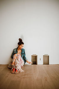 Woman sitting on hardwood floor against wall