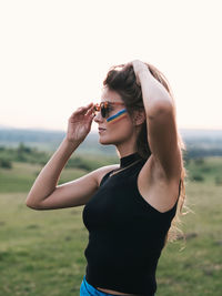 Close-up of a woman with a rainbow on her cheek and hands holding glasses and hair