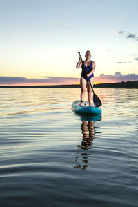 Rear view of woman swimming in sea against sky during sunset