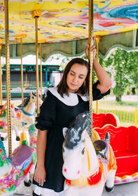 Beautiful brunette girl in a black dress poses on a bright carousel with horses