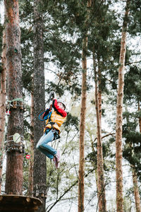 Low angle view of girl zip lining in forest 