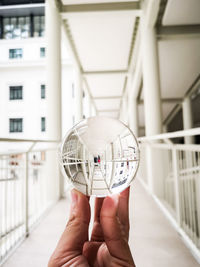 Cropped hand of person holding crystal ball against building
