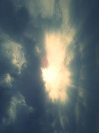 Low angle view of sunlight streaming through clouds