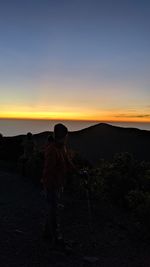 Rear view of woman standing on rock against sky during sunset