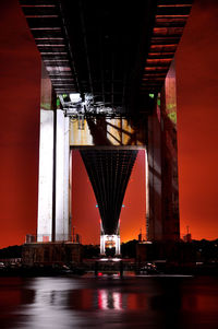 Illuminated city by sea against sky at night