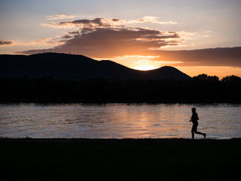 Silhouette woman running at lakeshore against mountains