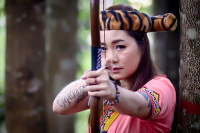 Portrait of young woman holding longbow outdoors