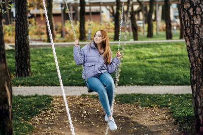 Candid portrait of beautiful young woman on swing on spring day outdoors. happy student teenager