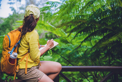 Midsection of woman sitting on railing against trees