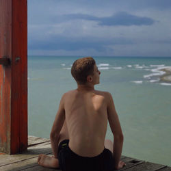 Rear view of shirtless man looking at sea against sky