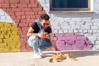 Full length of a young man standing against brick wall