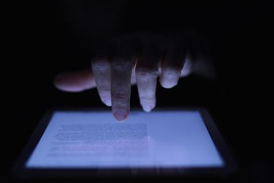 Close-up of hand holding book over black background