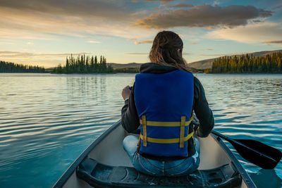 Rear view of woman sitting on boat in lake against sky