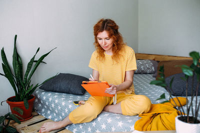 Woman working from home on bed using graphics tablet for design and drawing