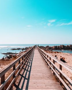 View of wooden footbridge leading towards sea against sky