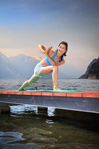 Full length of woman exercising on pier over river against sky