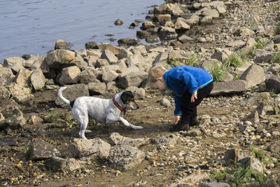 Side view of little boy playing with dog on lakeshore