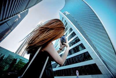 Low angle view of woman against modern buildings in city