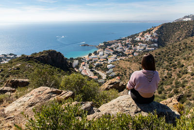 Rear view of woman looking at sea while sitting on rock