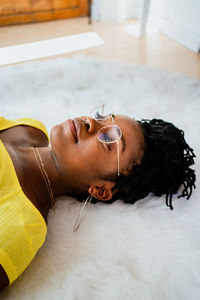 From above of african american female in casual clothes and eyeglasses lying on soft carpet while resting at home